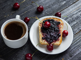White Cup of coffee and toast with cherry jam on white plate on black table