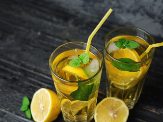 Traditional iced, lemon and mint iced tea . Mojito in two glass glasses on a dark concrete table