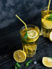 Traditional iced, lemon and mint iced tea . Mojito in two glass glasses on a dark concrete table