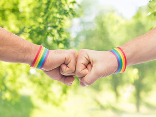 lgbt, same-sex love and homosexual relationships concept - close up of male couple hands with gay pride rainbow awareness wristbands making fist bump gesture over green natural background