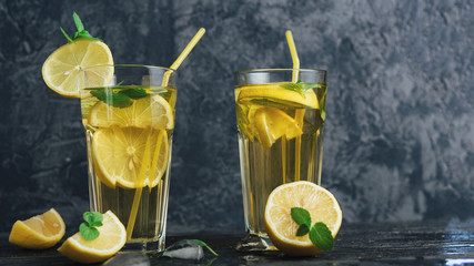Traditional iced, lemon and mint iced tea . Mojito in two glass glasses on a dark concrete table copyspace