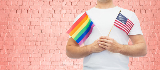 lgbt, same-sex relationships and homosexual concept - close up of man wearing gay pride rainbow awareness wristband and holding american flag over pink brick wall background
