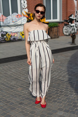 Fototapeta na wymiar Asian Chinese model girl influencer street shot. Wearing striped white dress jumpsuit. Street Graffiti background.