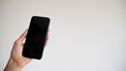A woman's left hand holds blank black phone on a white background