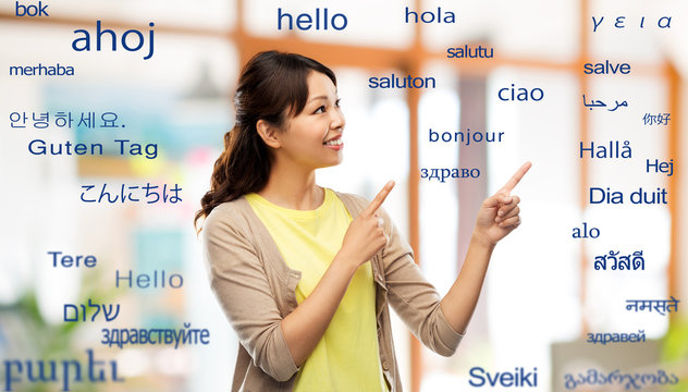 translation, education and people concept - happy asian young woman pointing fingers up over greeting words in different foreign languages