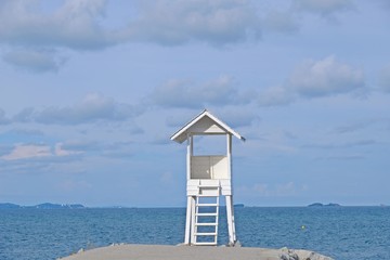 Little wooden white life guard tower at the sea at the center of frame with blue sky background, ...