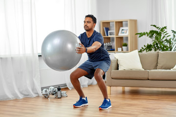 fitness, sport and healthy lifestyle concept - indian man exercising and doing squats with ball at...