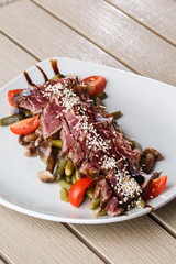 Sliced medium rare Roast beef with pickles, cherry tomatoes,mushrooms on a white plate on wooden background.