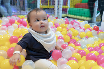 Fototapeta na wymiar Happy Asian baby girl playing in a big dry pond full with plastic balls, kid at indoor playground