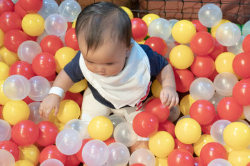 Fototapeta na wymiar Happy Asian baby girl playing in a big dry pond full with plastic balls, kid at indoor playground