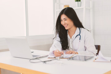 Asian female doctor sitting at hospital office desk giving all patient convenience online service advice and smiling write a prescription to order medical, health care and preventing disease concept.