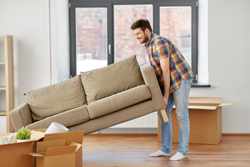 moving, people and real estate concept - happy man dragging sofa at new home