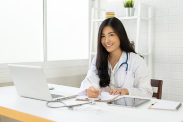 Asian female doctor sitting at hospital office desk giving all patient convenience online service advice and smiling write a prescription to order medical, health care and preventing disease concept.