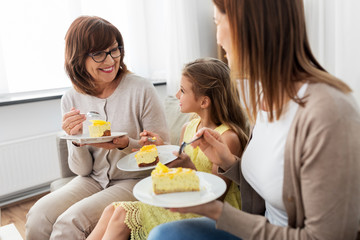 family, generation and food concept - smiling mother, daughter and grandmother eating cake at home