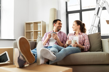moving, people, repair and real estate concept - happy couple sitting on sofa and drinking coffee at new home