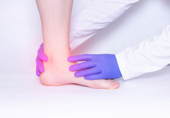 The doctor conducts a medical examination of the patient's ankle joint to detect arthritis and synovitis, trauma, luxation