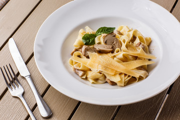 Tagliatelle vegetarian Pasta Dish with Mushrooms decorated with basil. Delicious lunch with pasta and white mushrooms. On wooden background.