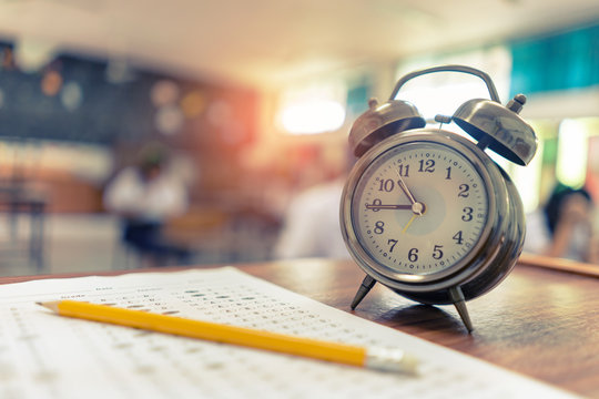 Test Examination in Education concept,pencil and Alarm clock on wooden table,students exams in a classroom background ,Scholarship tests for study abroad