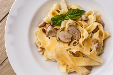 Tagliatelle vegetarian Pasta Dish with Mushrooms decorated with basil. Delicious lunch with pasta and white mushrooms. On wooden background.