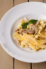 Tagliatelle vegetarian Pasta Dish with Mushrooms decorated with basil. Delicious lunch with pasta and white mushrooms. On wooden background.