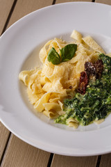 Tagliatelle vegetarian Pasta Dish with spinach and dried tomatoes decorated with basil. Delicious lunch with pasta and spinach. On wooden background.