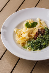 Tagliatelle vegetarian Pasta Dish with spinach and dried tomatoes decorated with basil. Delicious lunch with pasta and spinach. On wooden background.