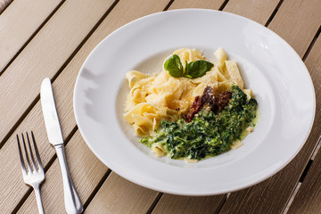 Tagliatelle vegetarian Pasta Dish with spinach and dried tomatoes decorated with basil. Delicious lunch with pasta and spinach. On wooden background.