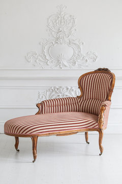 Vintage sofa with wood carvings in a luxurious light interior with stucco on the walls. Selective focus.
