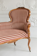 Vintage sofa with wood carvings in a luxurious light interior with stucco on the walls. Selective focus. Close up.