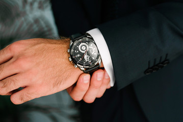 A man in a suit adjusts the clock on his hand close up.