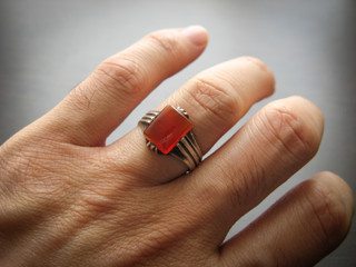 Yemeni red akik agate stone. Male hand with ring on ring finger with dark background.