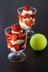 Whipped cream and strawberries served in a glass. Dark wooden table, tennis ball, high resolution