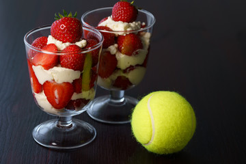 Whipped cream and strawberries served in a glass. Dark wooden table, tennis ball, high resolution