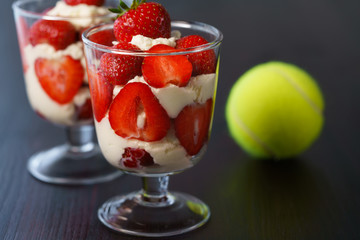 Whipped cream and strawberries served in a glass. Dark wooden table, tennis ball, high resolution
