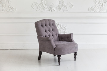 Living room in the Rococo style. Vintage grey armchair against the wall with plaster stucco patterns. Selective focus.