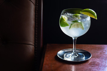 Cold Gin and Tonic (or Vodka) with Ice and Limes in Dark Luxurious Bar with Black Background