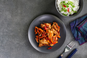 Teriyaki chicken with carrots and a bowl of rice on a dark background