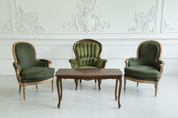 Vintage armchairs and coffee table against the wall with plaster stucco patterns. Selective focus.