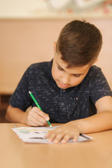 Naklejka na ściany i meble Concentrated schoolboy sitting at desk and writing in exercise book