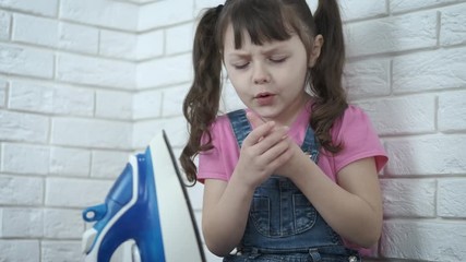 The child plays with a hot iron. The little girl burned her fingers on the hot iron. A child at home without parental control.