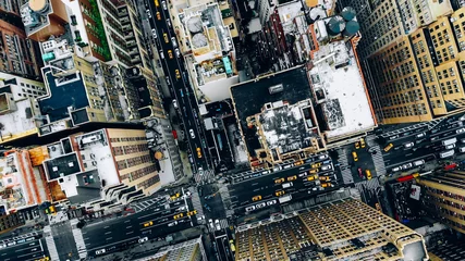 Fotobehang Luchtmening van de de bouwdaken van de binnenstad van New York. Vogelperspectief vanuit de helikopter van de stadsinfrastructuur van de metropool, verkeersauto& 39 s, gele taxi& 39 s die door de straten van de stad rijden en districtslanen oversteken © BullRun