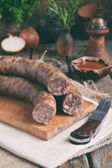 Obraz na płótnie Canvas Traditional smoked sausage in a rustic style. Appetizing sausages made of pork and lamb with fresh herbs, spices on the wooden board. Free space for text.