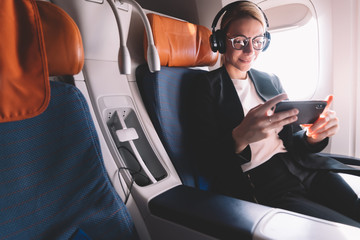 Caucasian girl in formal wear reading news from smartphone during flight in airplane sitting near...