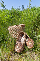 Braided bark sandals and braided birch bark box on the background of green grass and blue sky