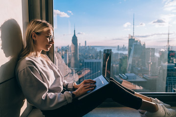 Caucasian female digital nomad keyboarding article for travel blog while working on laptop computer...