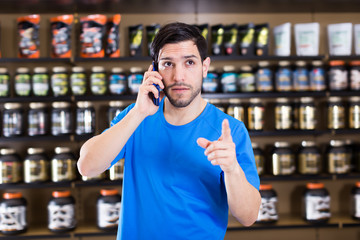 Young  man talking by phone near shelves in shop