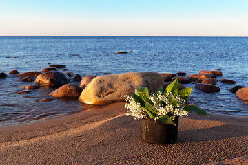 Bouquet of lily of the valley in the tourist sooty pot on a sandy beach by the lake at sunset