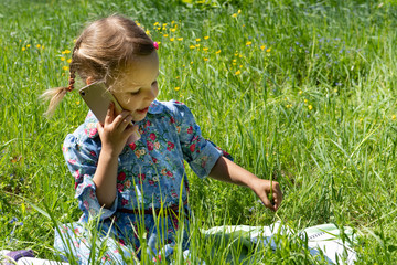 Happy little girl talking on the phone on the green lawn.