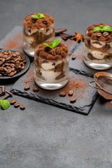Classic tiramisu dessert in a glass on stone serving board on dark concrete background