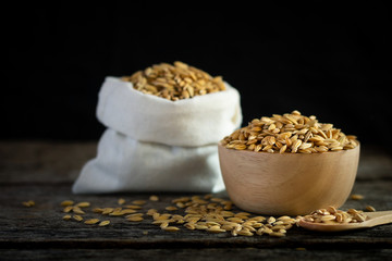 Closeup of  paddy rice in wooden bowl with paddy rice in sack on old wooden board